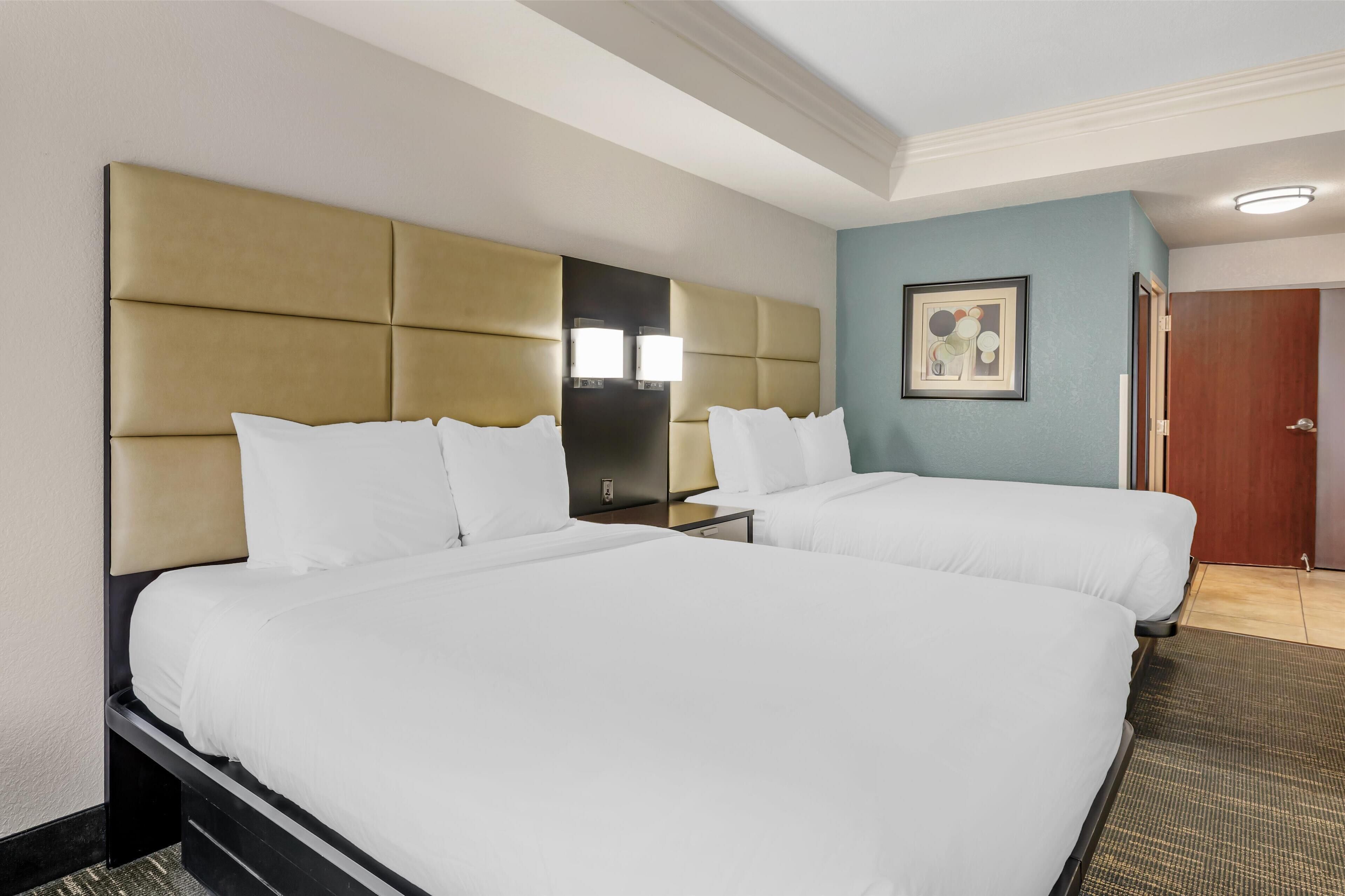 A hotel room with two beds, a large headboard, a nightstand, a framed picture on the wall, and a door.
