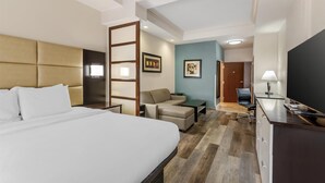 A hotel room with a bed, a sofa, a desk, a TV, and a door leading to a hallway. - Best Western Plus JFK Inn & Suites (North Little Rock)