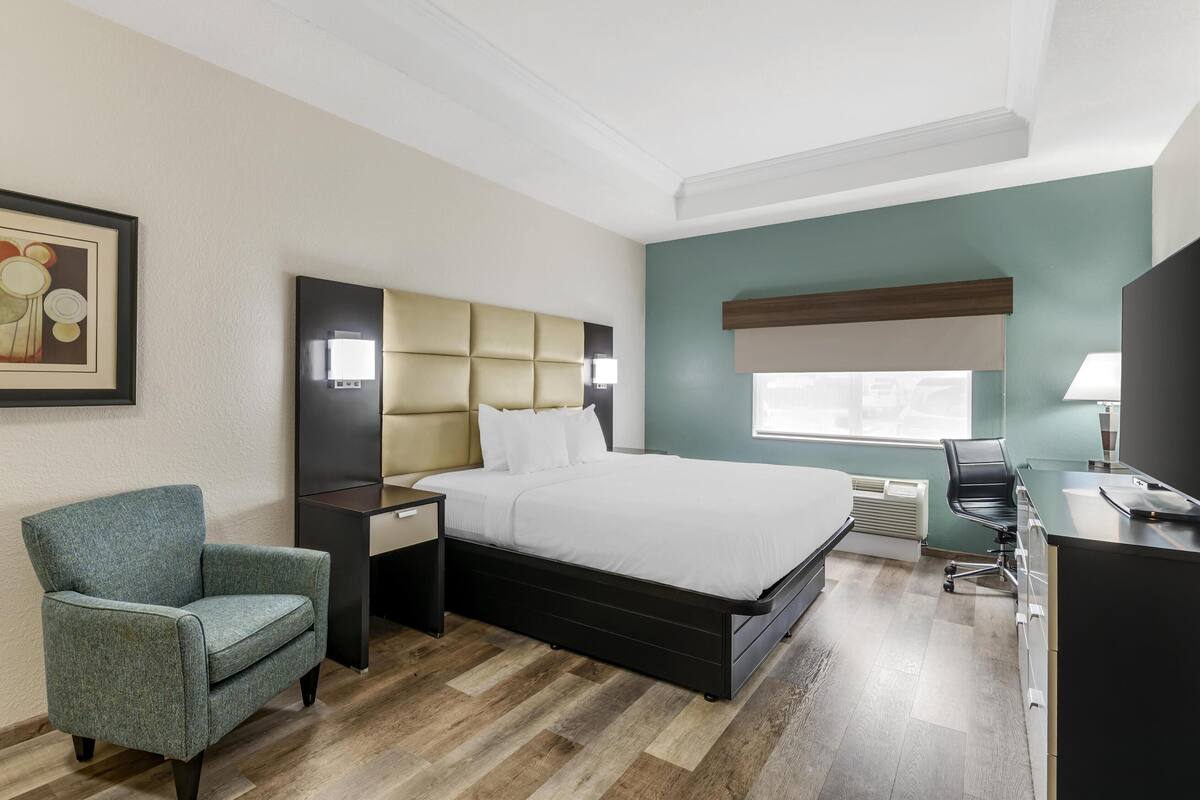 A hotel room with a bed, a chair, a desk, and a window.