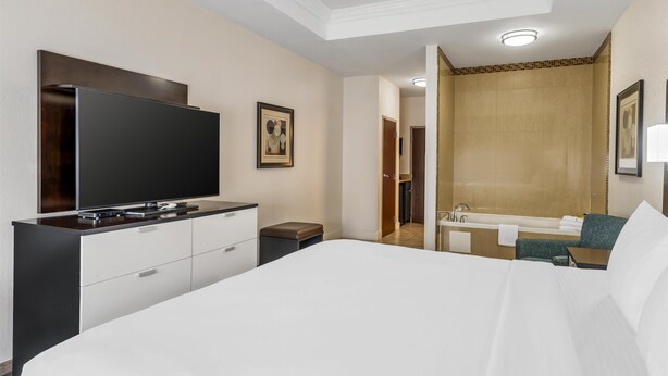 A modern hotel room with a large bed, a flat-screen TV, a desk, and a bathroom with a bathtub. - Best Western Plus JFK Inn & Suites (North Little Rock)