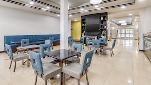 A modern dining area with tables and chairs, a blue sofa, and a kitchen area in the background. - Best Western Plus JFK Inn & Suites (North Little Rock)