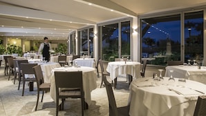 A restaurant with round tables and chairs, large windows, and a waiter walking.