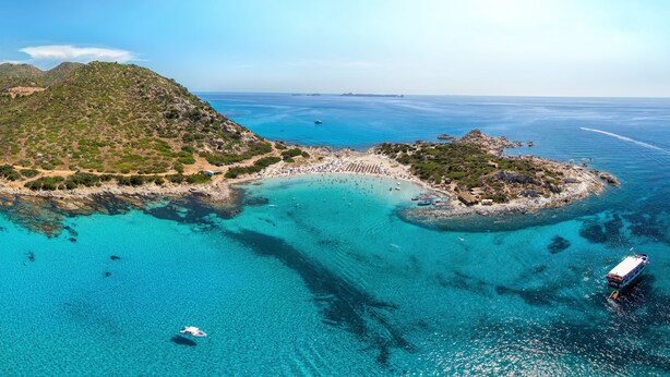 An aerial view of a coastal area with clear turquoise waters, a beach, and a small island with vegetation.