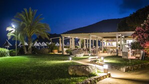 An outdoor dining area with tables and chairs, a covered seating area, and a pathway leading to the entrance.