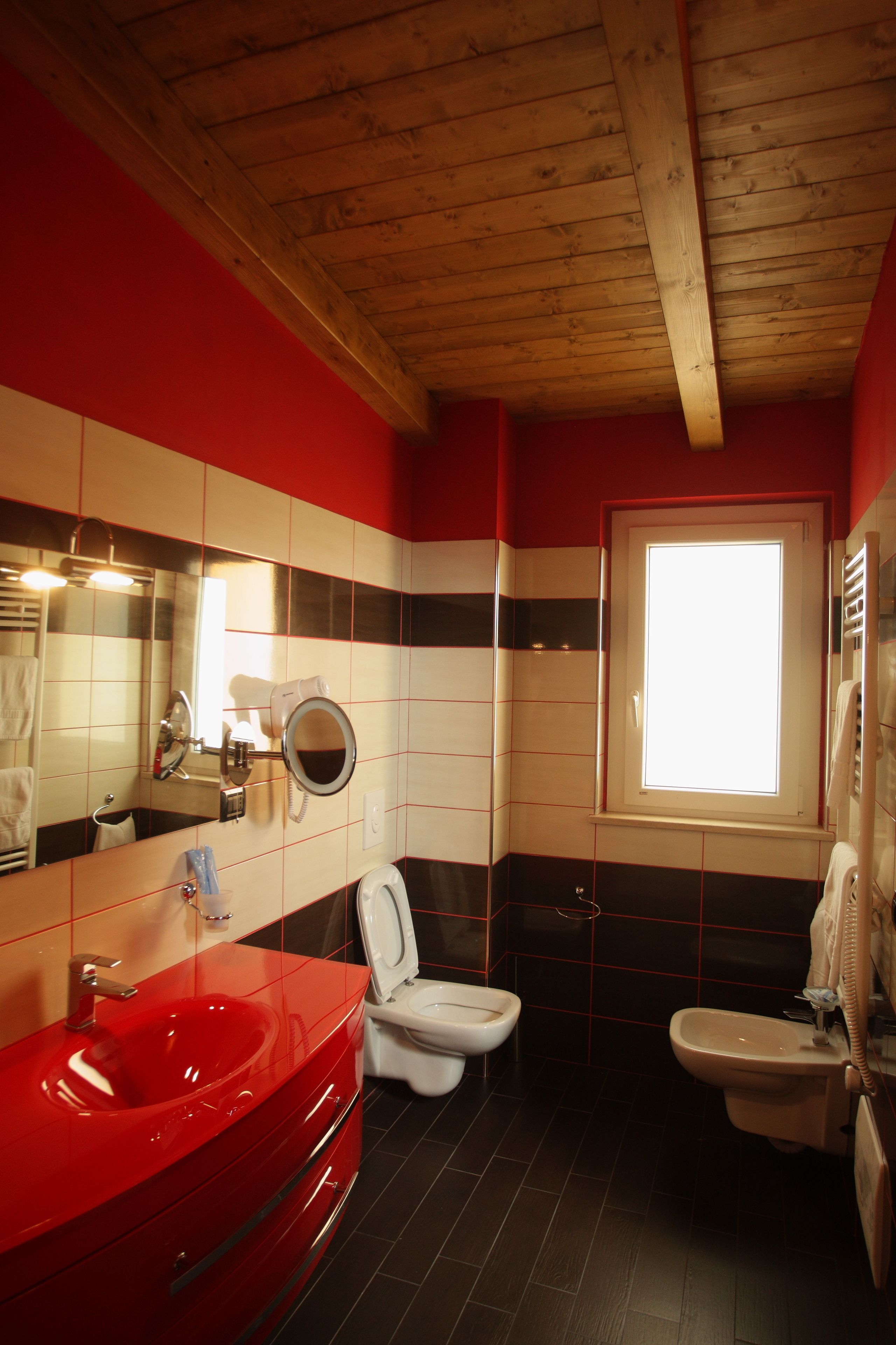 A bathroom with a red sink, white toilet, and a window.