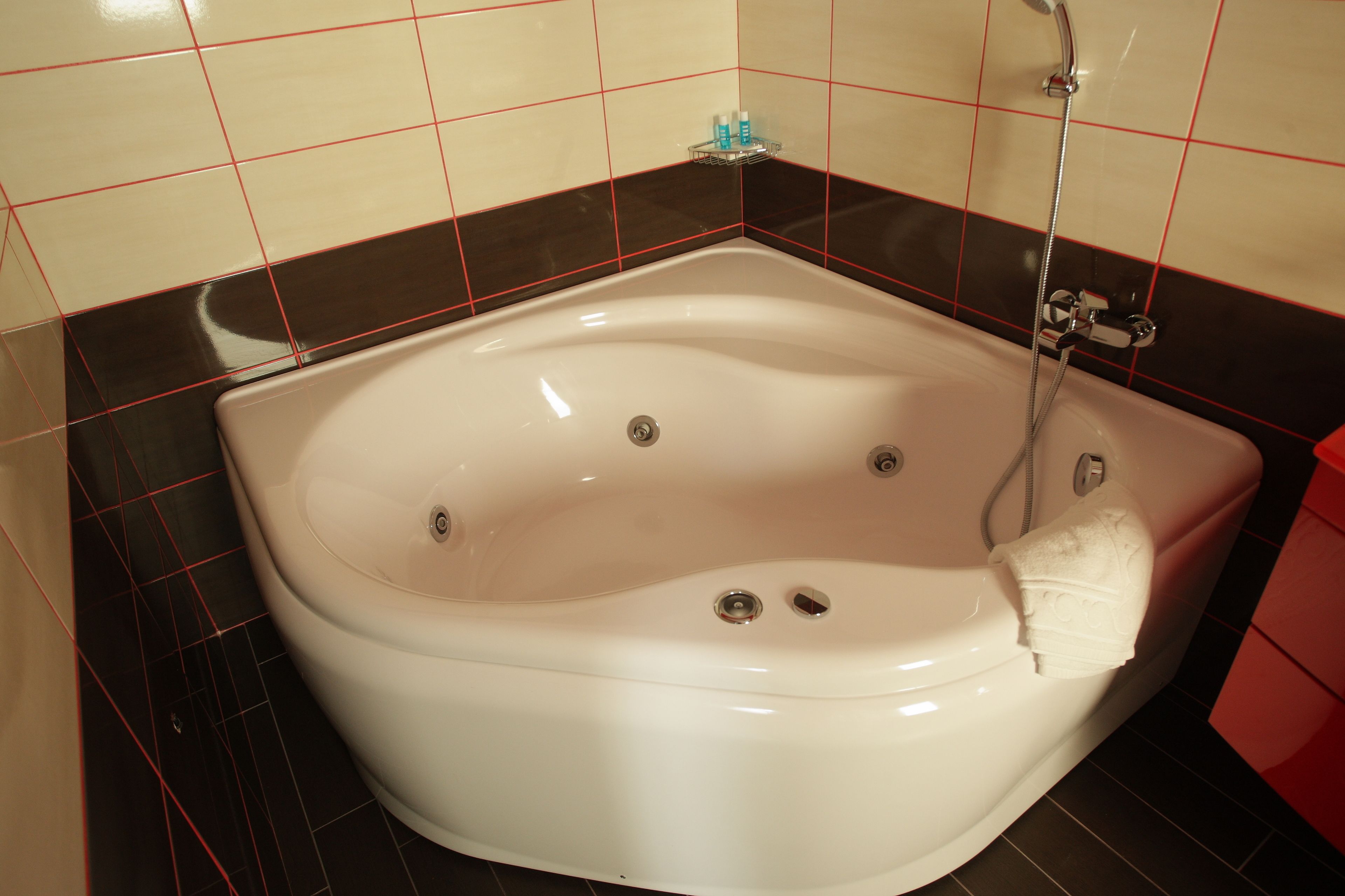 Una bañera blanca con ducha de mano, desagüe integrado y un pequeño estante con artículos de aseo.