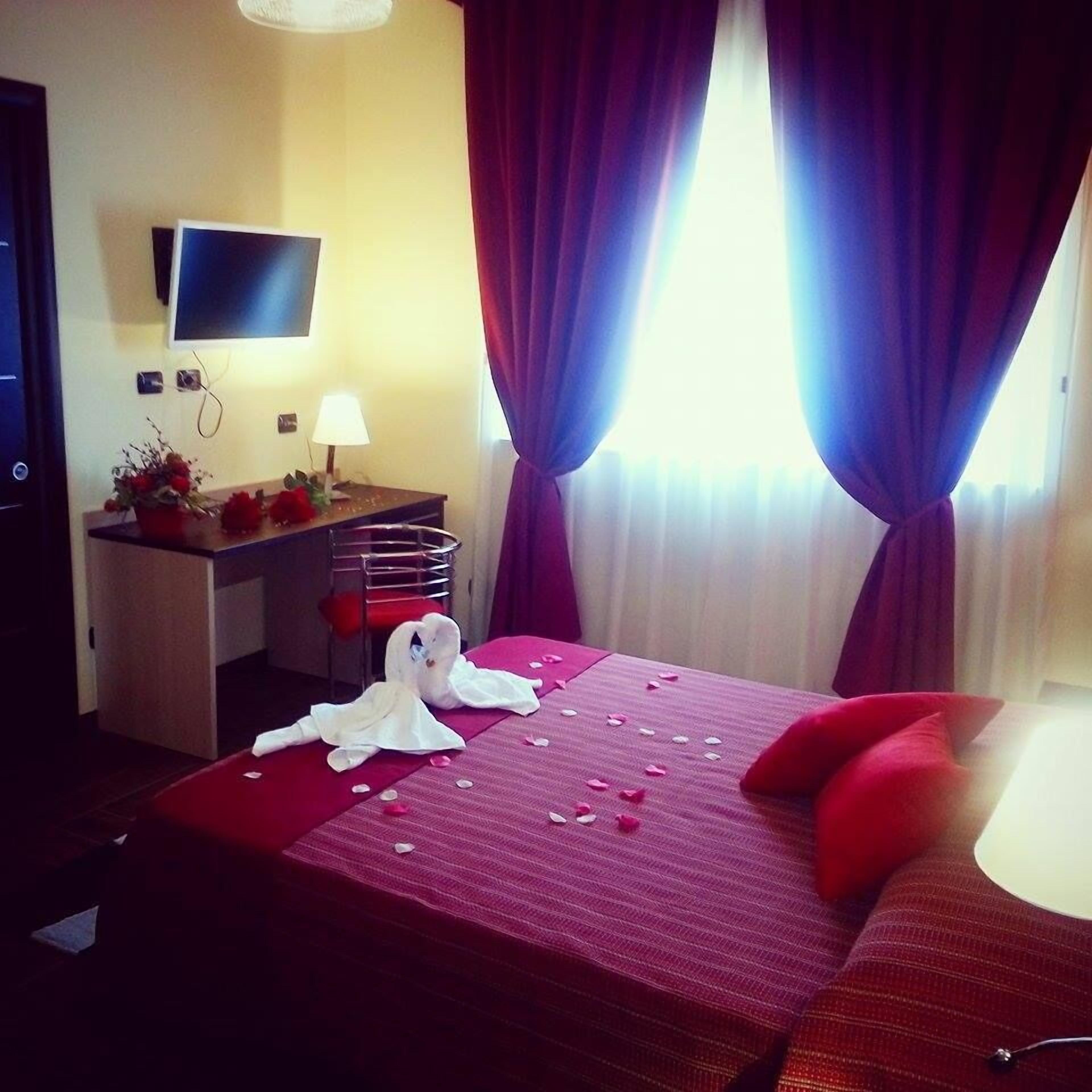 A hotel room with a bed, a desk, a chair, a TV, and a window with curtains.