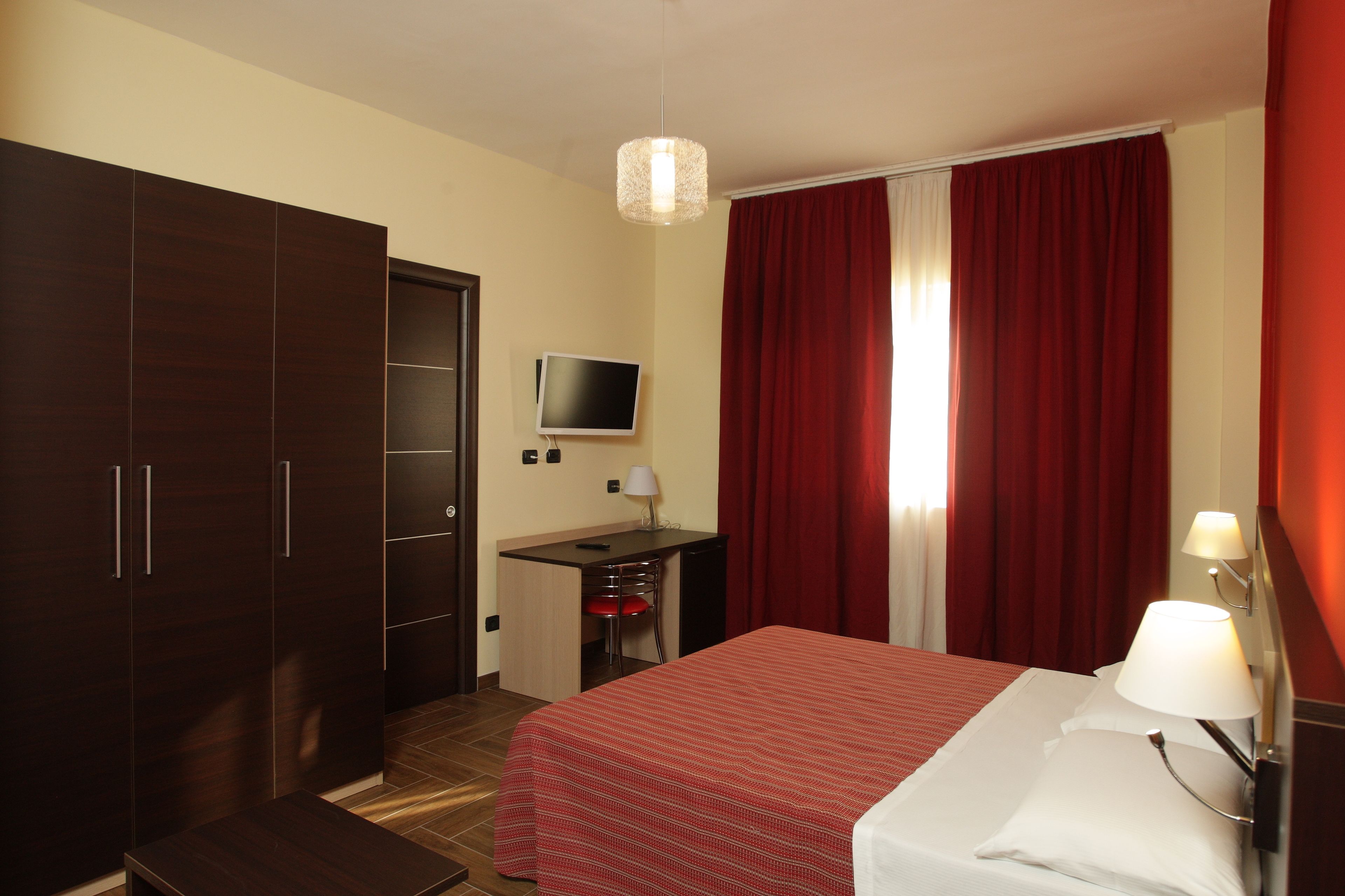 Una habitación de hotel con cama, escritorio, televisor y armario.