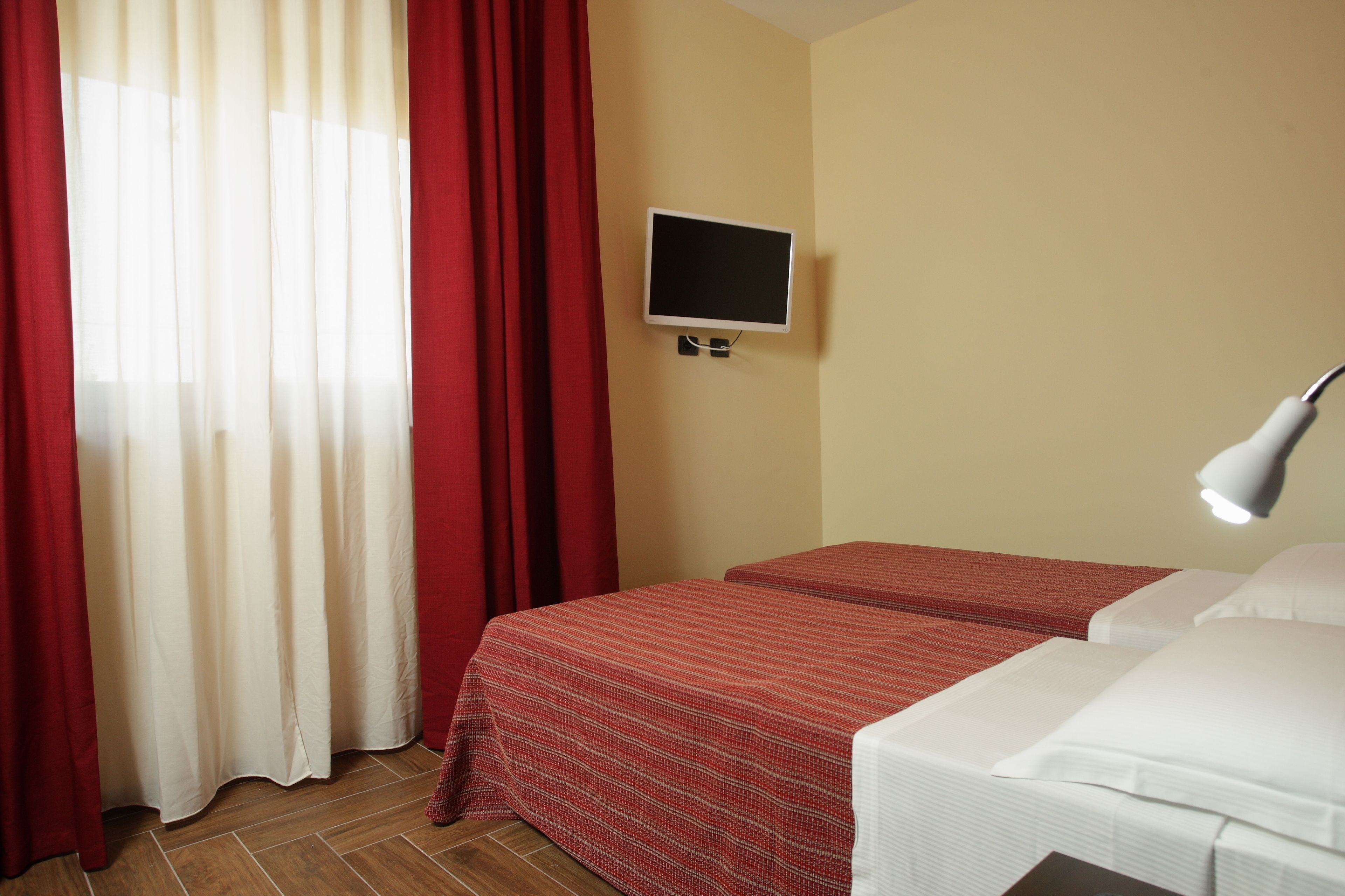 A hotel room with two beds, a TV on the wall, and a window with red curtains.
