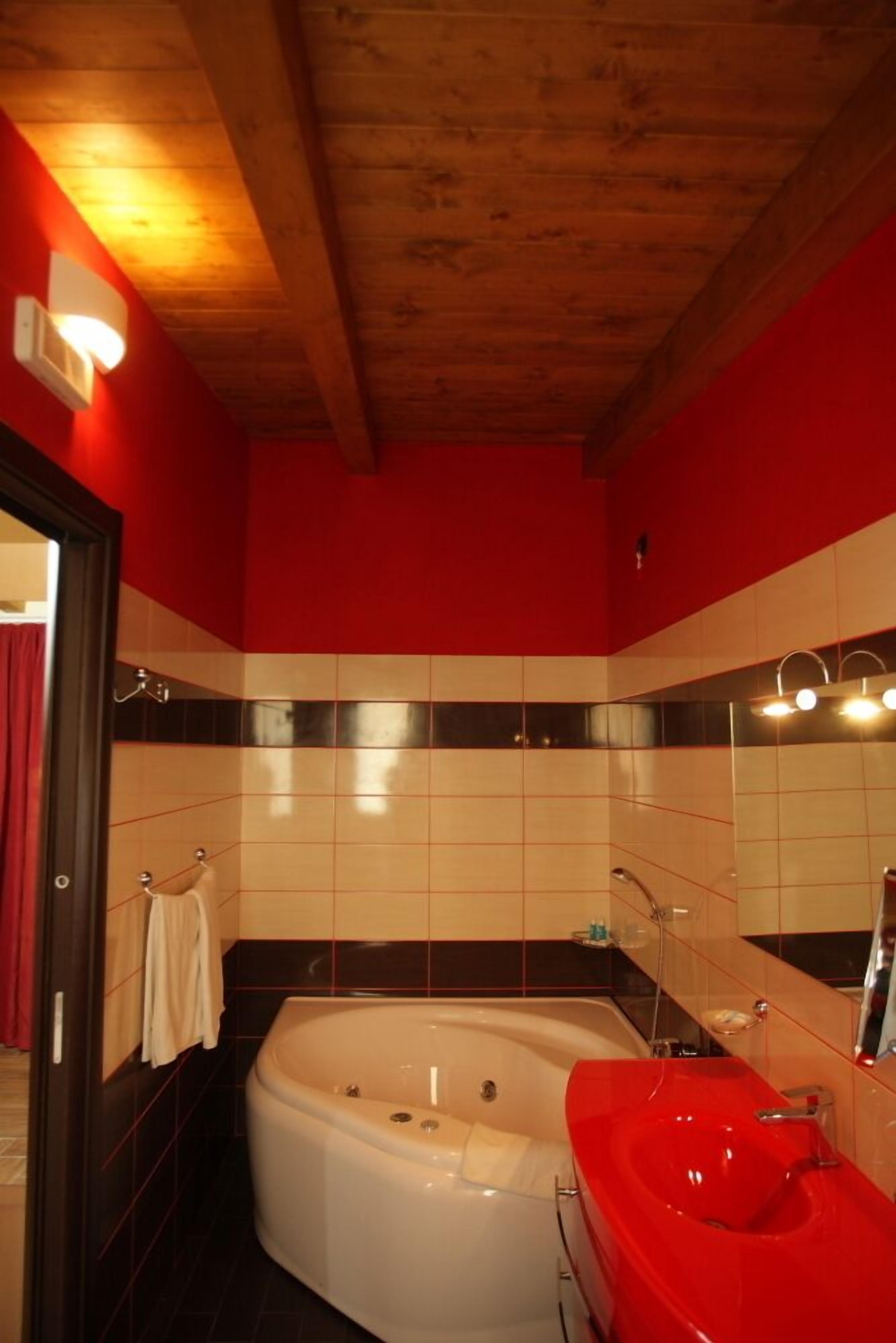 Un bany amb una banyera blanca, un lavabo vermell i un sostre de fusta.