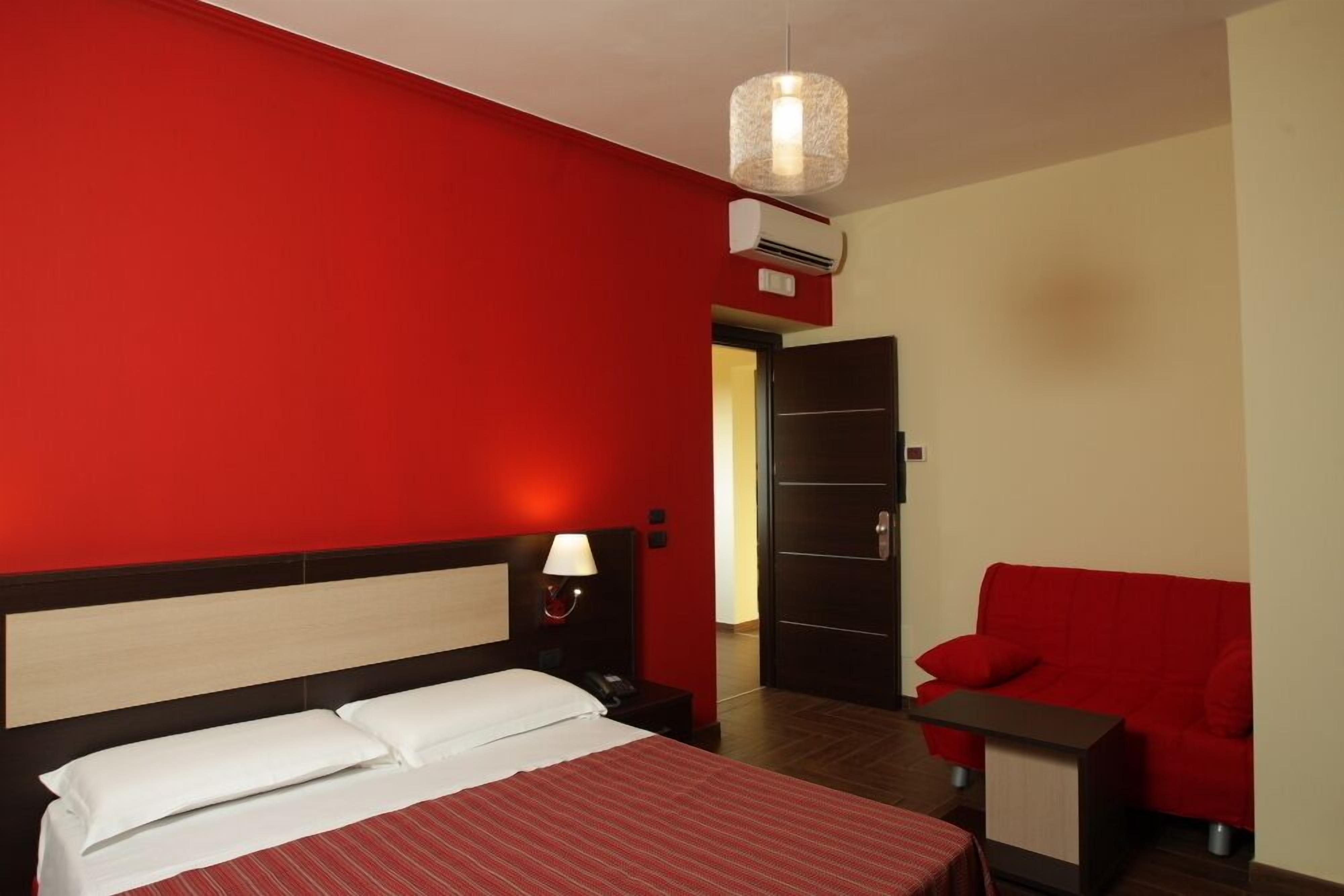 A hotel room with a red and white color scheme, a bed with white linens, a red sofa, a small table, and a hanging light fixture.