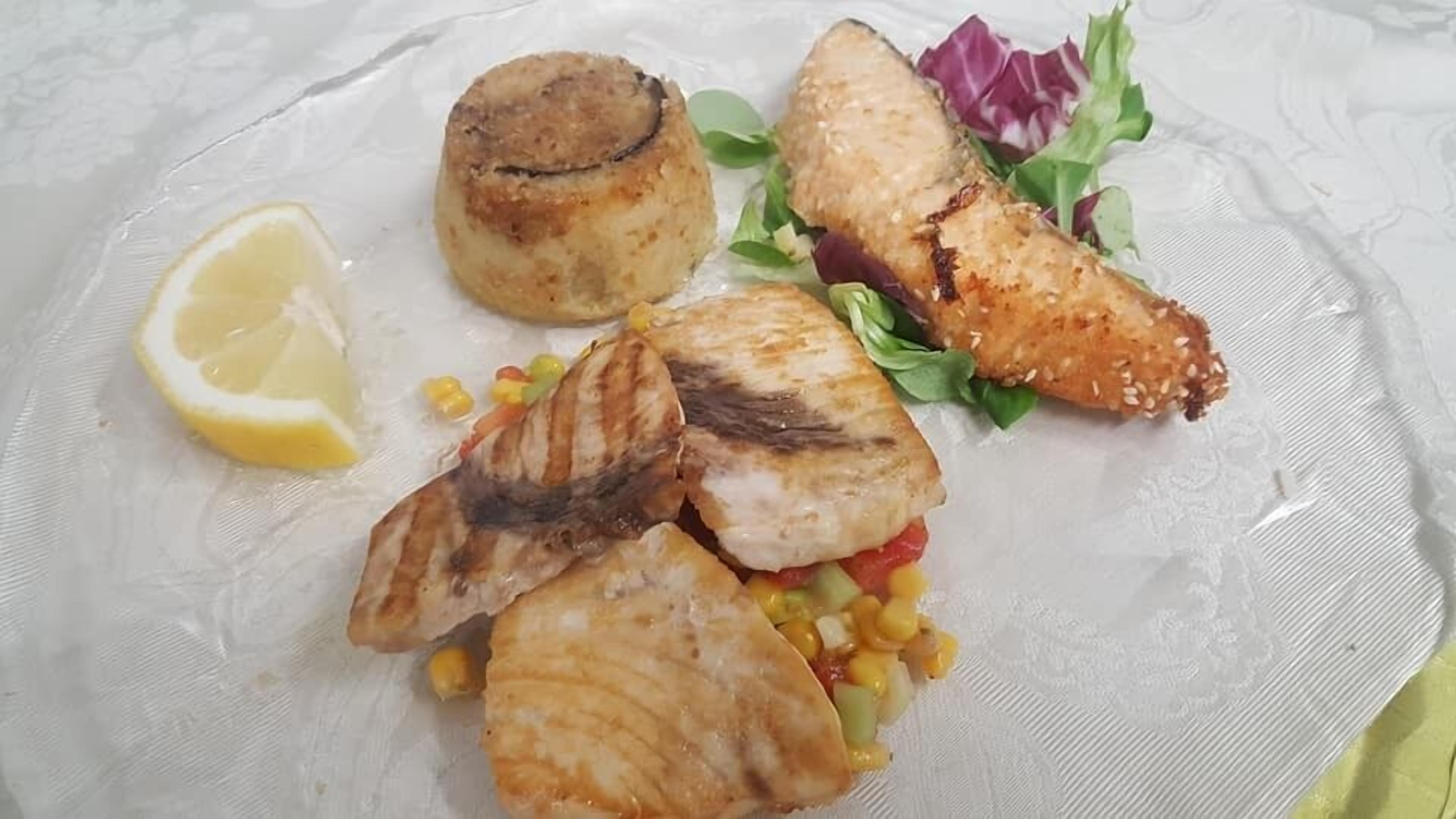 Une assiette contenant du poisson grillé, du maïs, un quartier de citron et une salade.