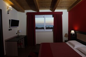 A hotel room with a bed, a desk with a computer, a TV, and a window with curtains. - Hotel Paradiso (Gizzeria)