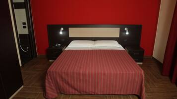 Una camera d'albergo con una parete rossa, un letto con copriletto a righe, due comodini con lampade e un pavimento in legno.
