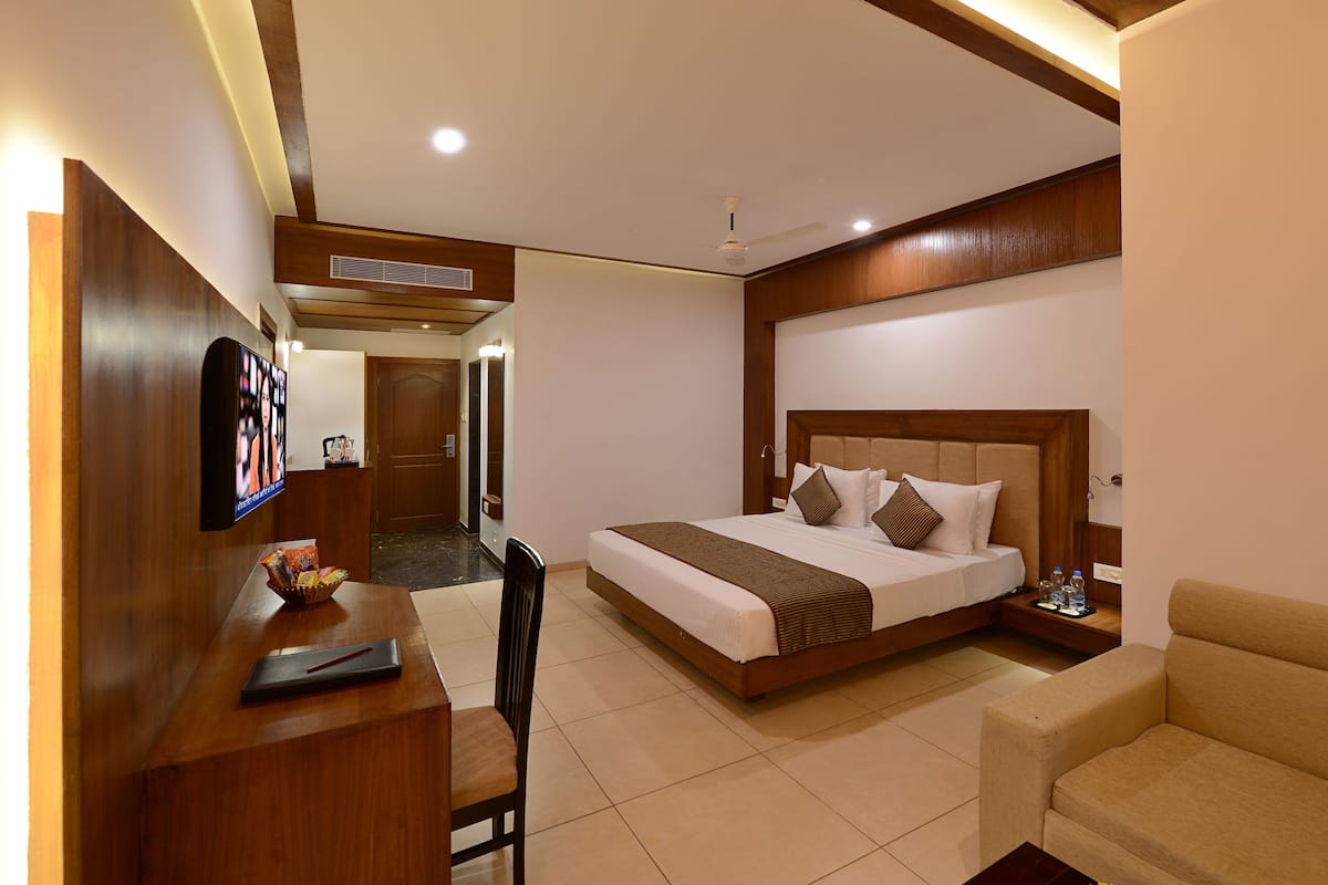 A hotel room with a bed, a desk, a chair, a sofa, and a television on the wall.