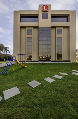 A building with a large logo at the top, a playground with slides and swings, and a well-maintained lawn with stepping stones.