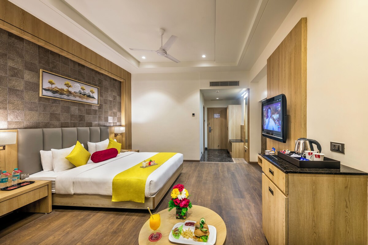 Habitación de hotel con cama, mesita de noche, televisión y una pequeña cocina.
