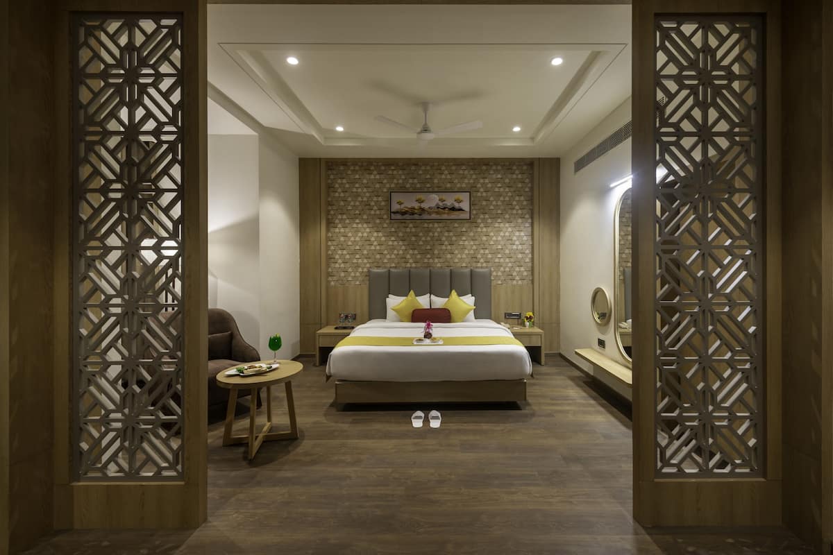 A modern hotel room with a large bed, a bedside table, a chair, and a decorative wall panel.