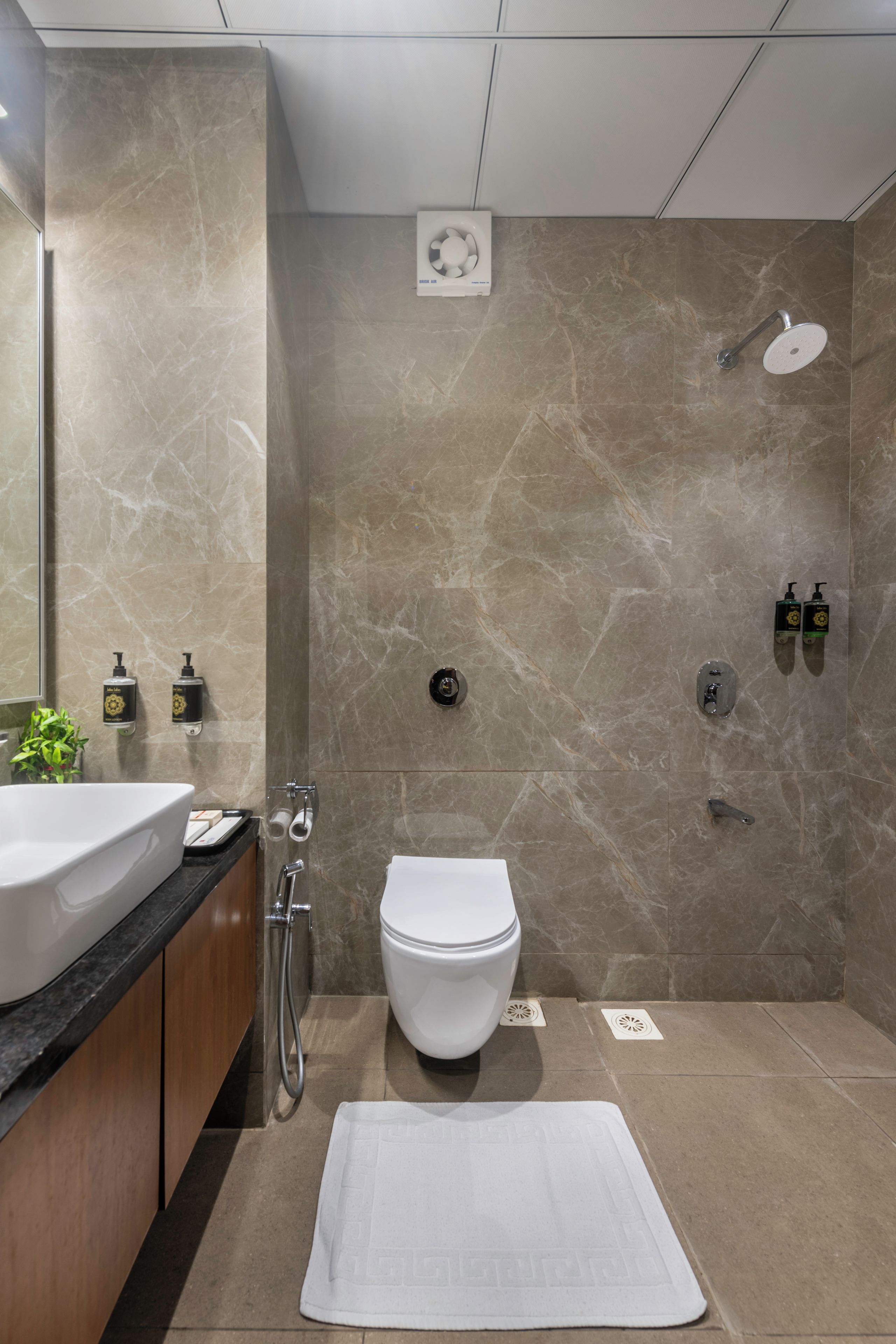 A modern bathroom with a marble wall, a toilet, a bidet, a shower, and a sink with a mirror.
