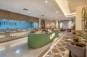 Vestíbulo de hotel con zona de buffet central, disposición de asientos y una pared decorativa.