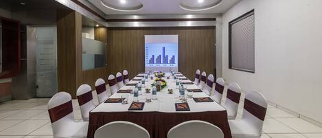 A conference room with a long table, white chairs with brown sashes, and a presentation screen at the front.