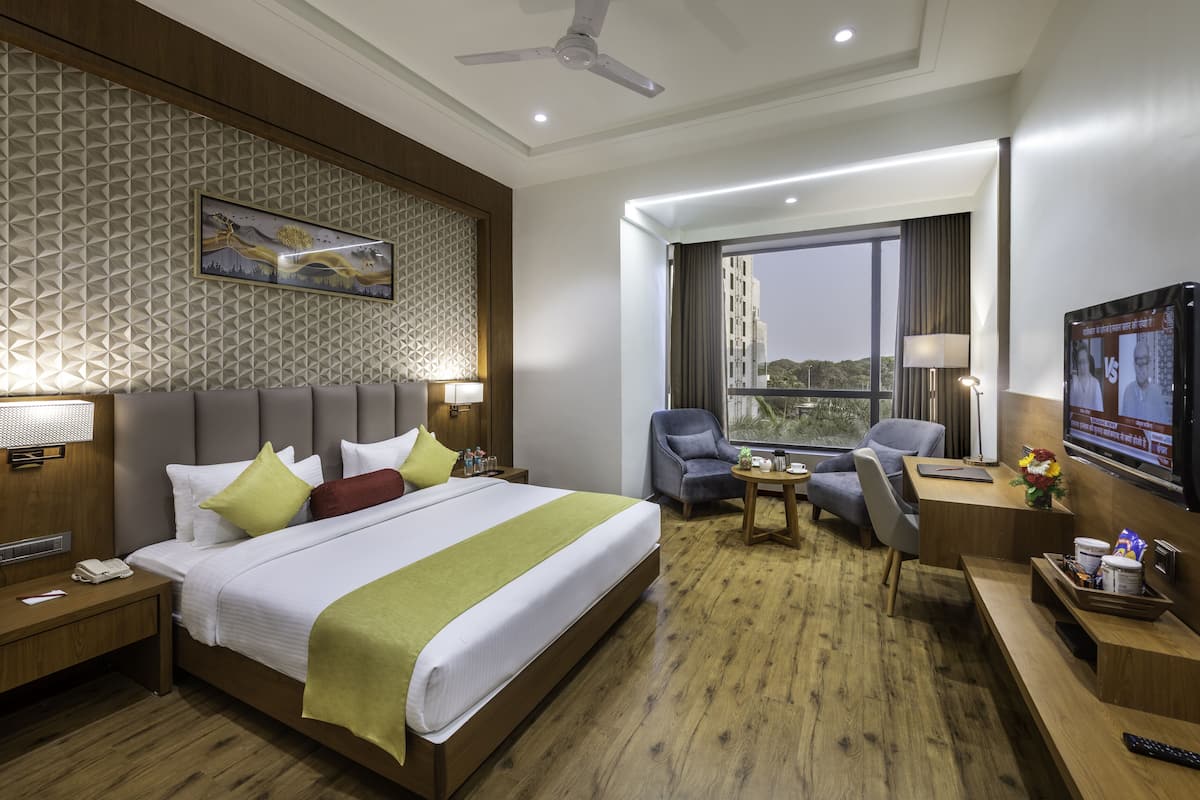 A hotel room with a large bed, a desk with a chair, a television, and a window with a view.