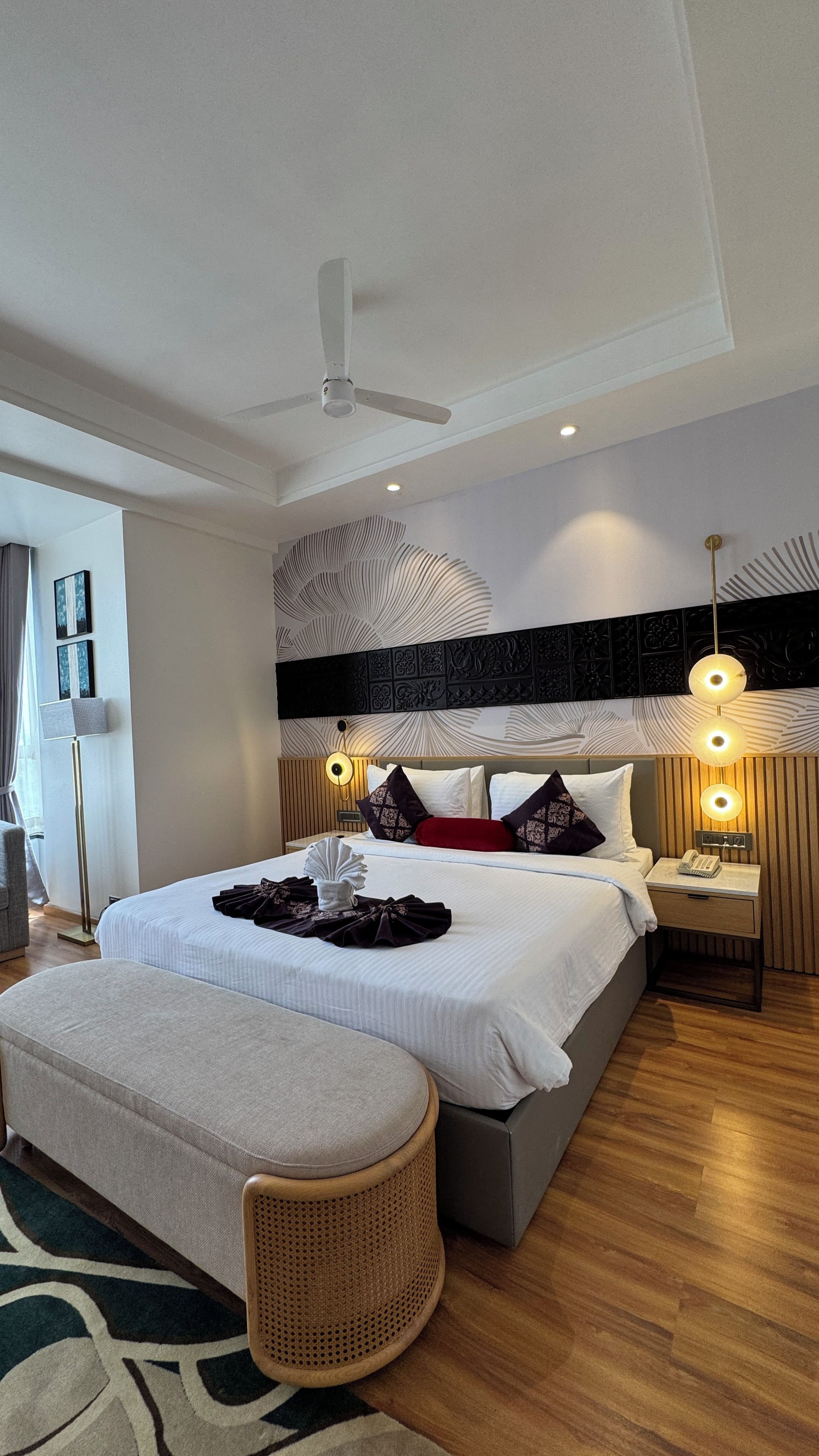 Une chambre d’hôtel moderne avec un grand lit, des lampes de chevet, un ventilateur de plafond et un panneau décoratif mural.