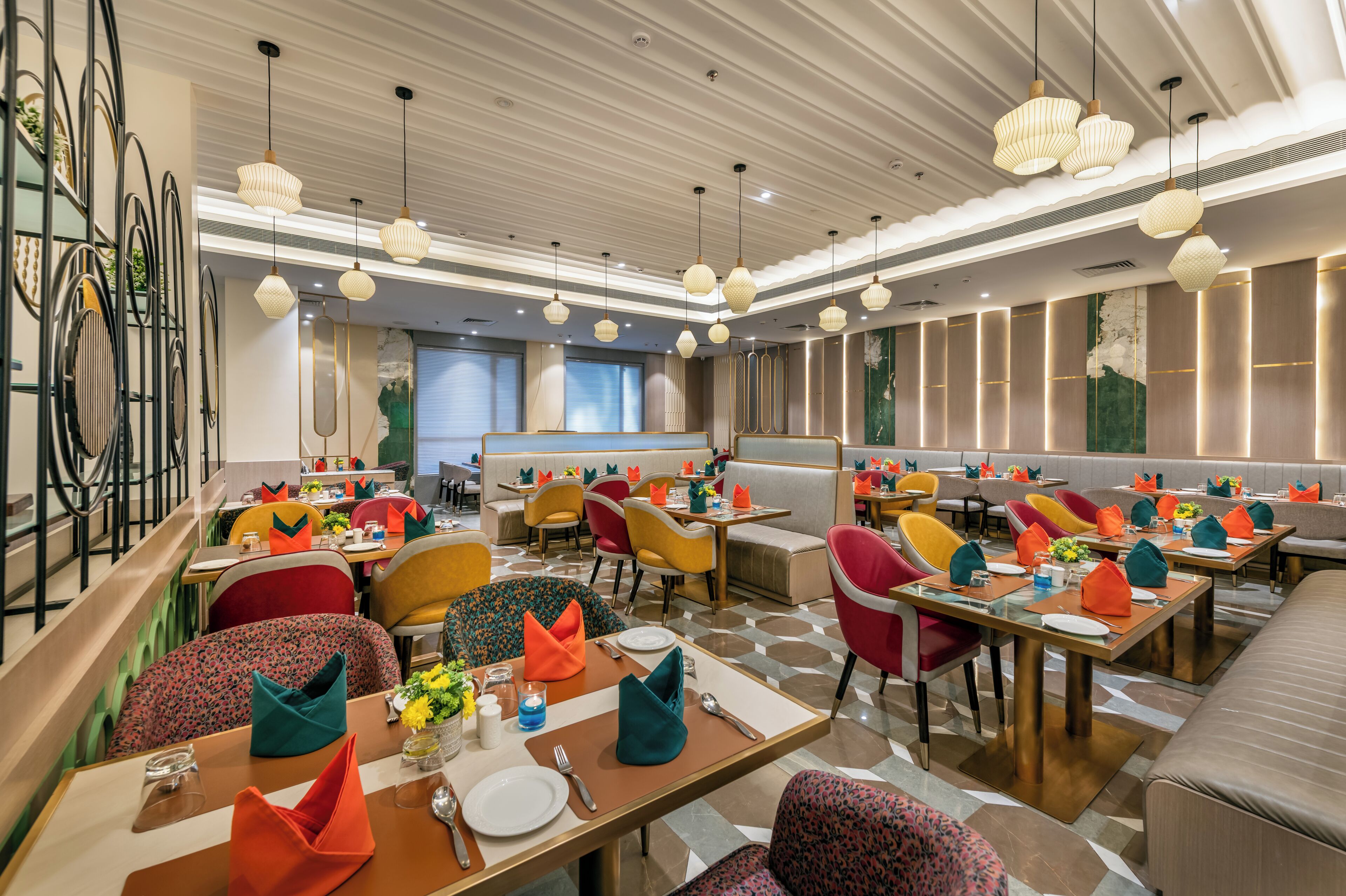 A modern restaurant interior with multiple dining tables, colorful chairs, and pendant lighting.
