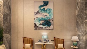 A lobby with two armchairs, a table, a lamp, and a large abstract painting on the wall.