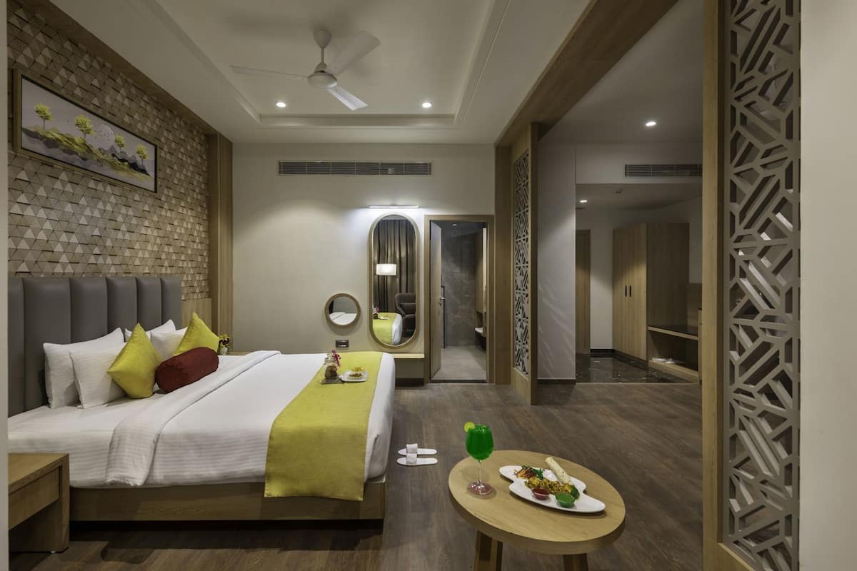 A modern hotel room with a bed, a small table with a meal, a bathroom, and a mirror.
