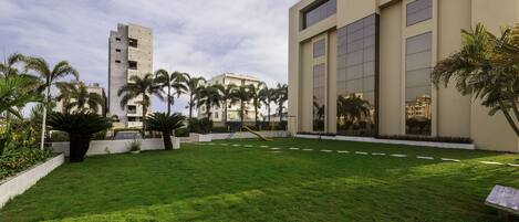 Un hotel con césped cuidado, palmeras y un parque infantil.