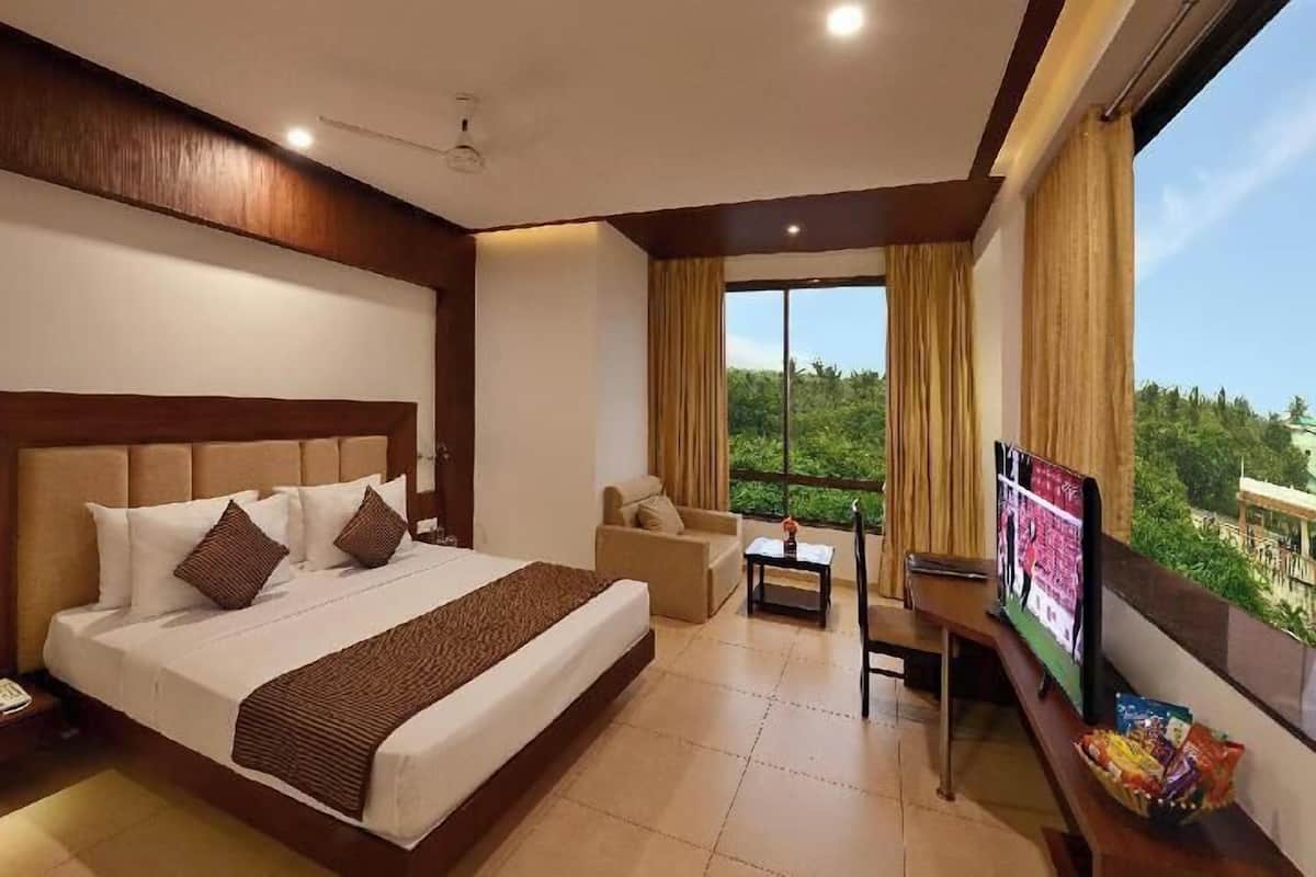 A hotel room with a large bed, a TV, a desk, and a balcony with a view.