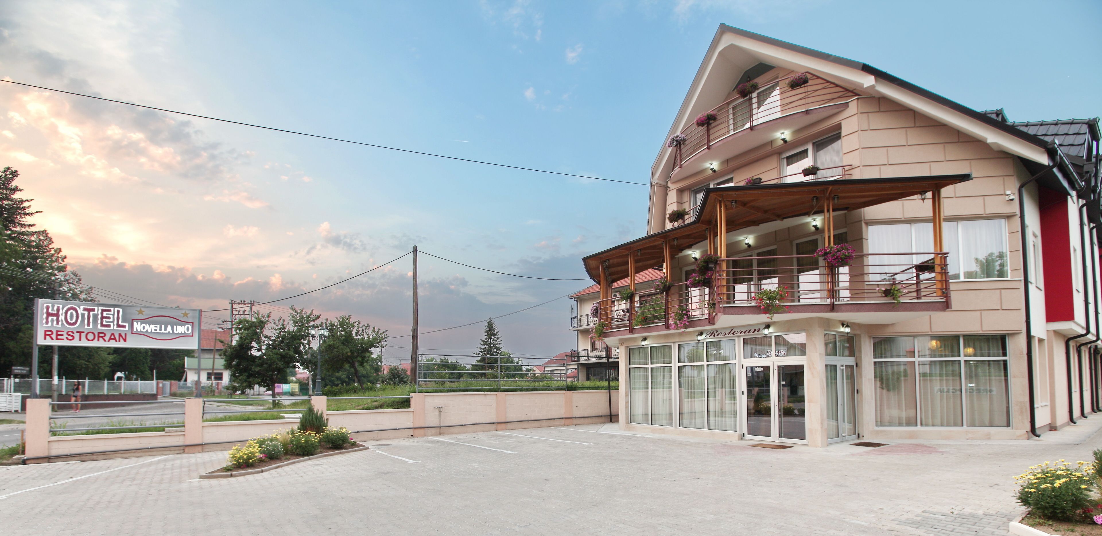 Un hotel con un grande cartello, diversi balconi con fioriere e un parcheggio.