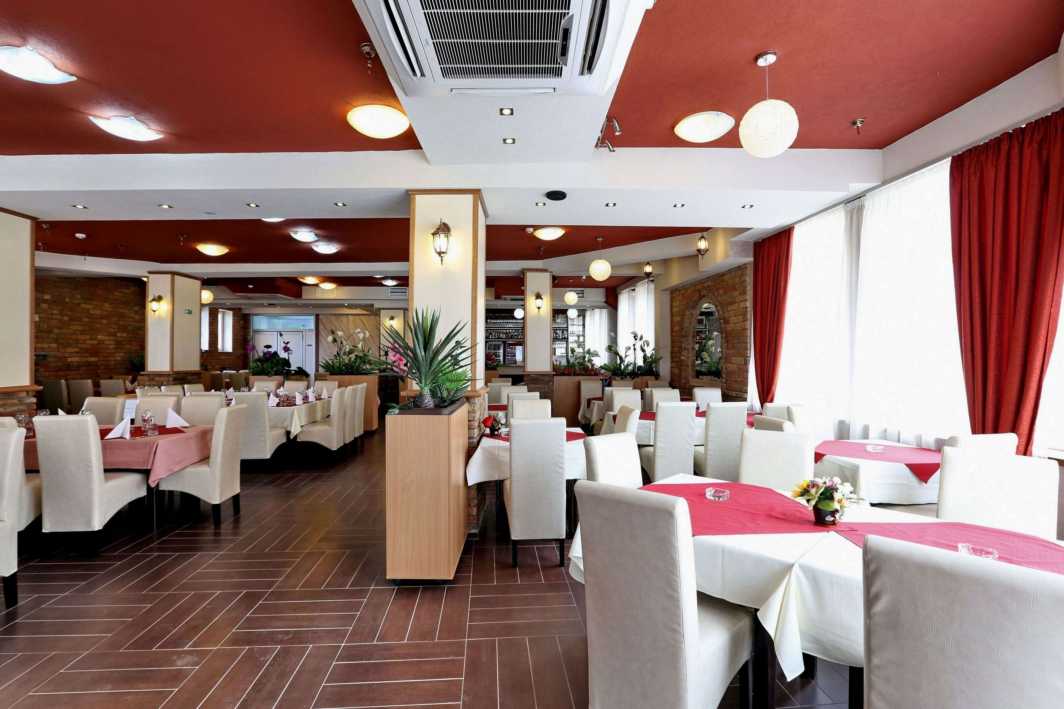 A spacious restaurant with multiple dining tables, red curtains, and a brick wall in the background.