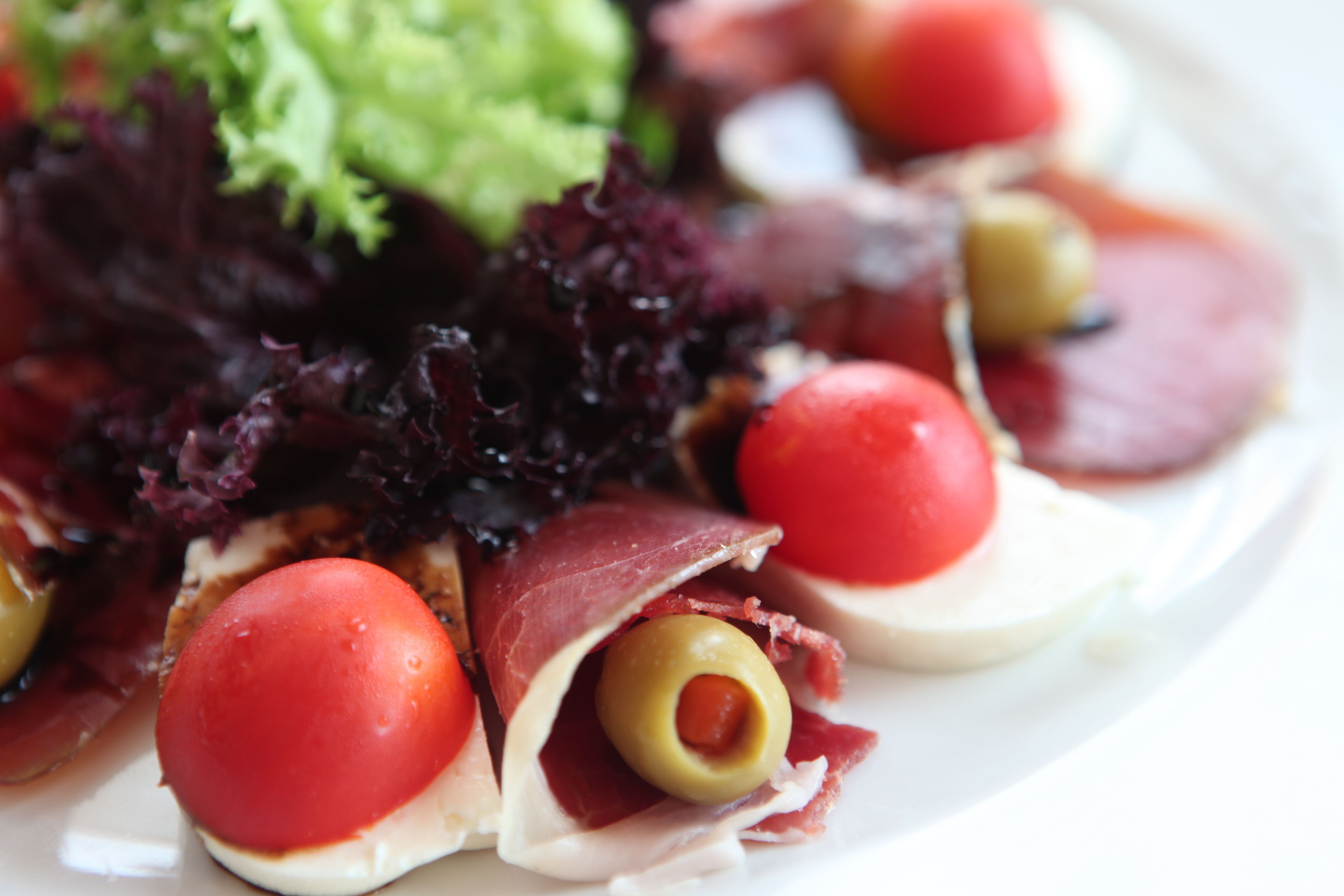 A plate of food with prosciutto, olives, and red tomatoes.