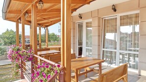 A covered outdoor seating area with wooden tables and benches, a railing with flowers, and large windows. - Hotel Novella Uno (Novi Banovci)