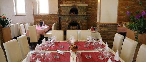 A dining area with tables set for a meal, a brick fireplace, and a view of the dining area.