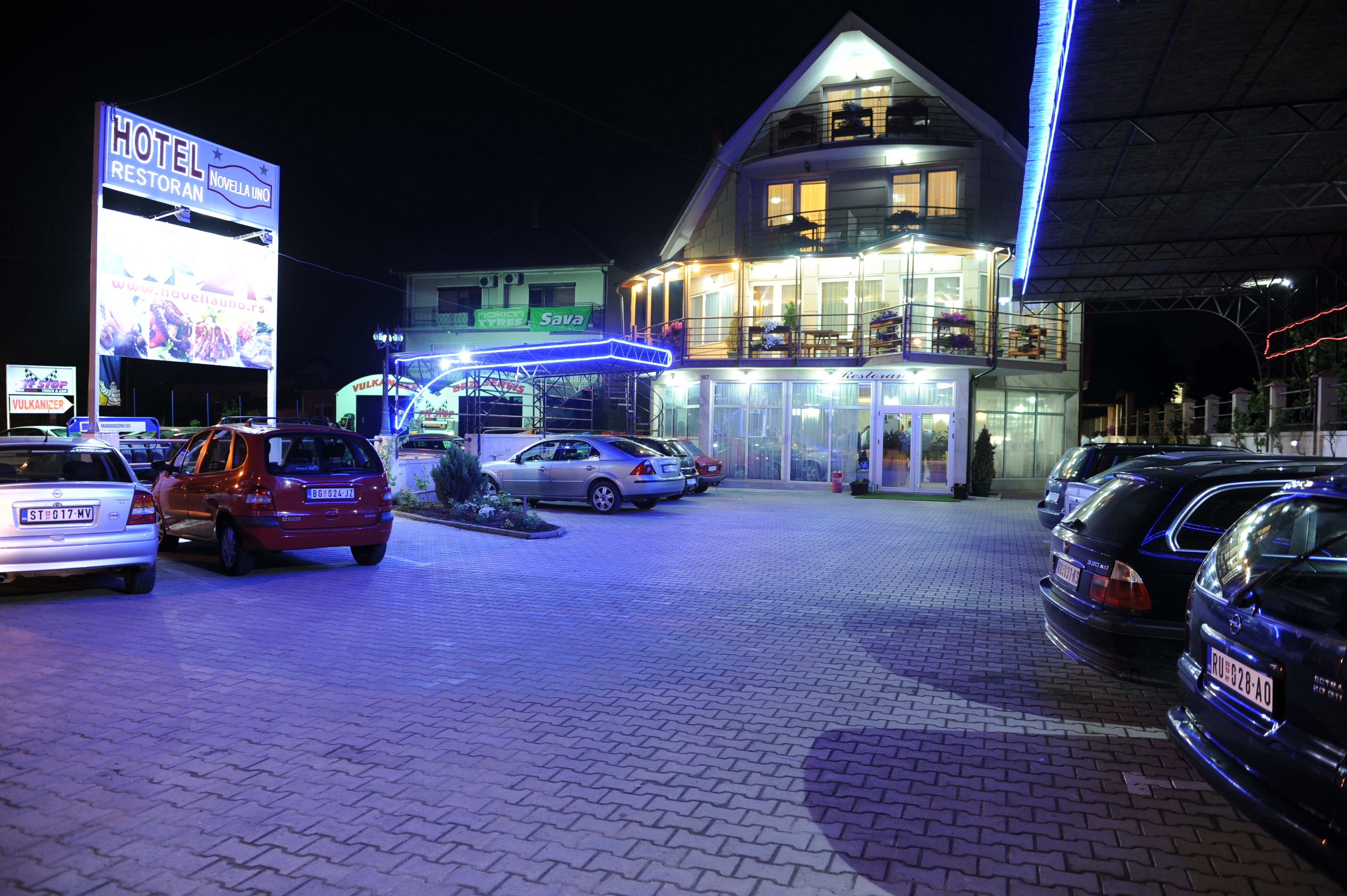 Un hotel con un cartel iluminado grande, un estacionamiento con varios coches y una entrada bien iluminada.