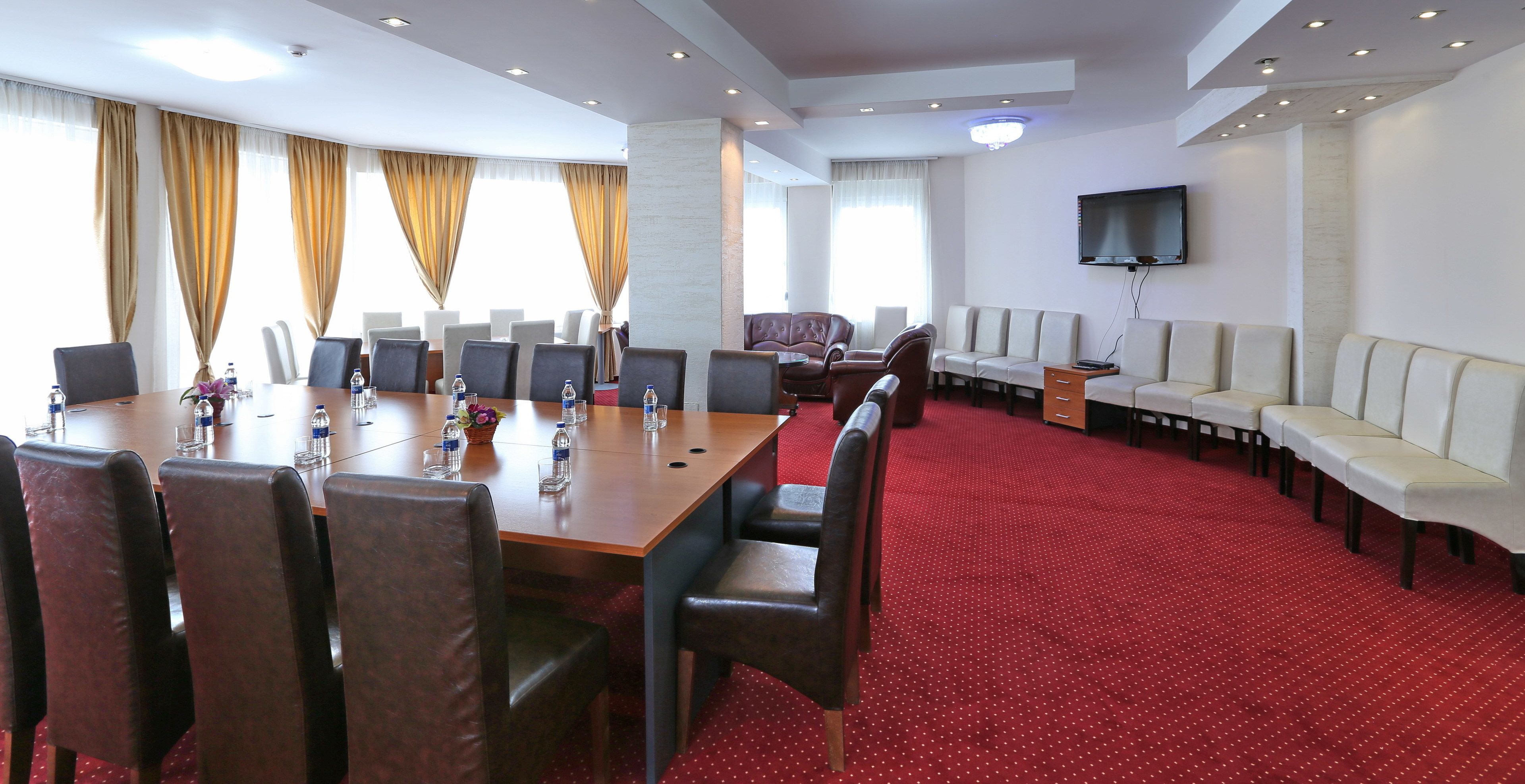 A conference room with a long table, chairs, a sofa, and a TV.