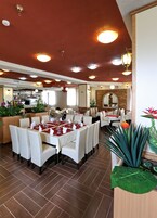 Um restaurante com várias mesas dispostas para os clientes, uma área de cozinha ao fundo e uma parede de tijolos com um espelho.