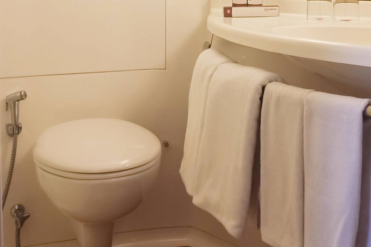 A bathroom with a toilet, a shower, and a sink with a towel hanging on the wall.