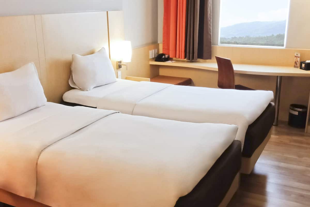 A hotel room with two beds, a desk, a chair, and a window with curtains.