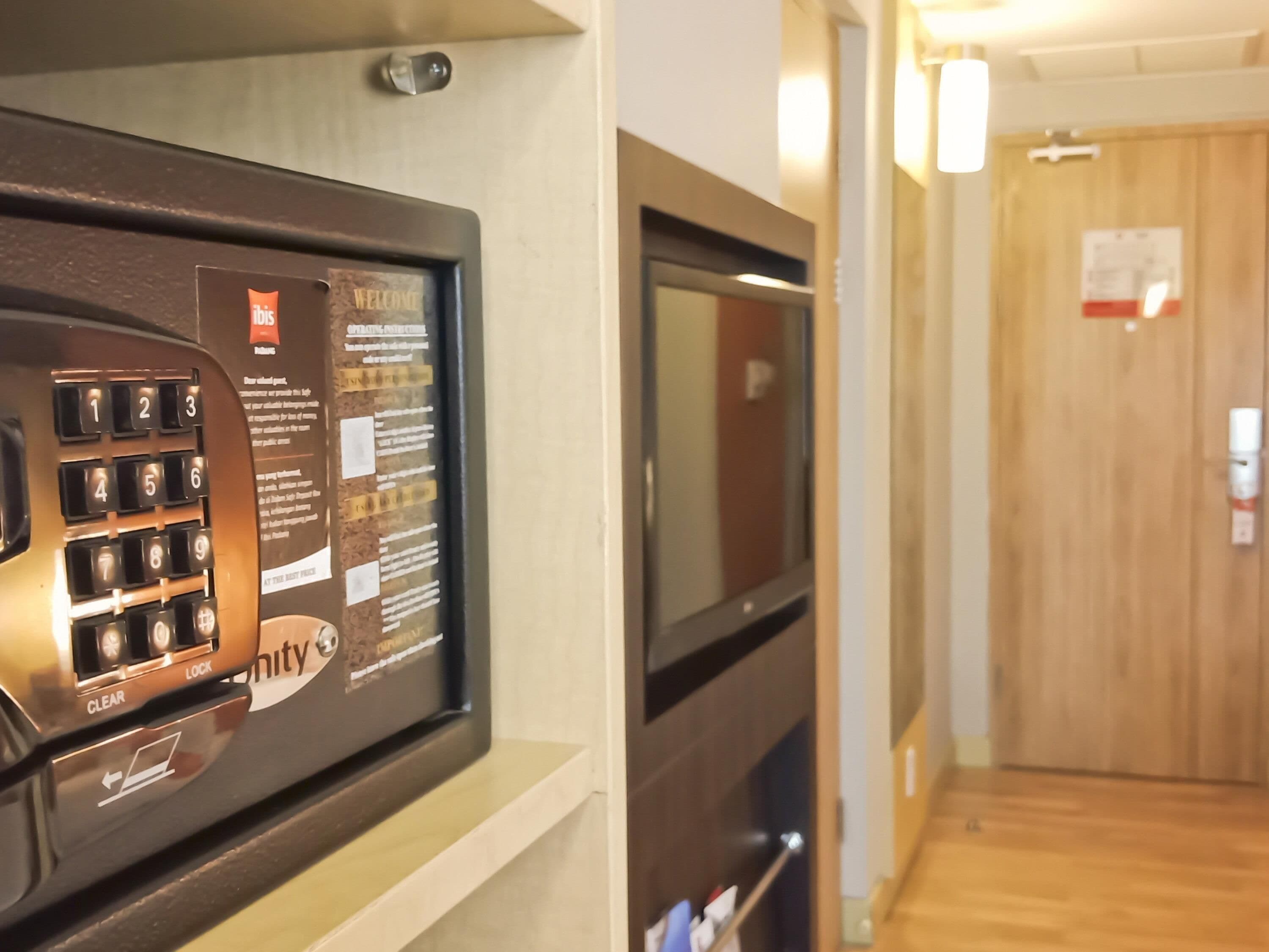 Een hotel receptie met een keypad voor toegang tot de kamers, een digitaal scherm en een houten deur op de achtergrond.