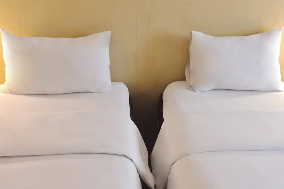 Two single beds with white bedding against a plain wall.