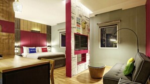 A modern hotel room with a bed, a desk, a sofa, a TV, and a decorative wall. - ibis Padang Hotel (Padang)