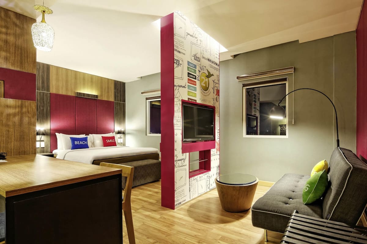 A modern hotel room with a bed, a desk, a sofa, a TV, and a decorative wall.