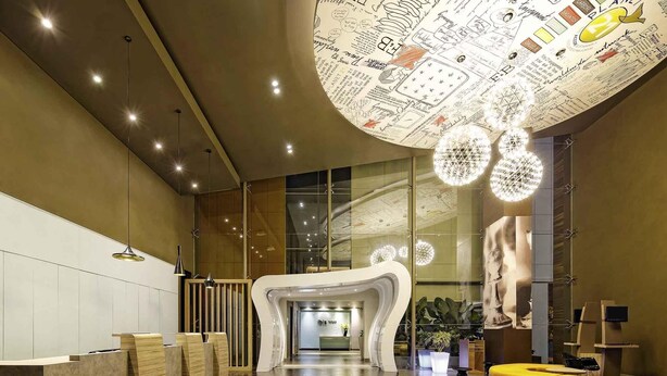 A modern lobby with a reception desk, seating area, and a unique ceiling design. - ibis Padang Hotel (Padang)
