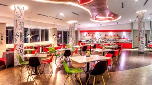 A modern restaurant interior with a unique ceiling design, multiple dining tables, and colorful chairs. - ibis Padang Hotel (Padang)