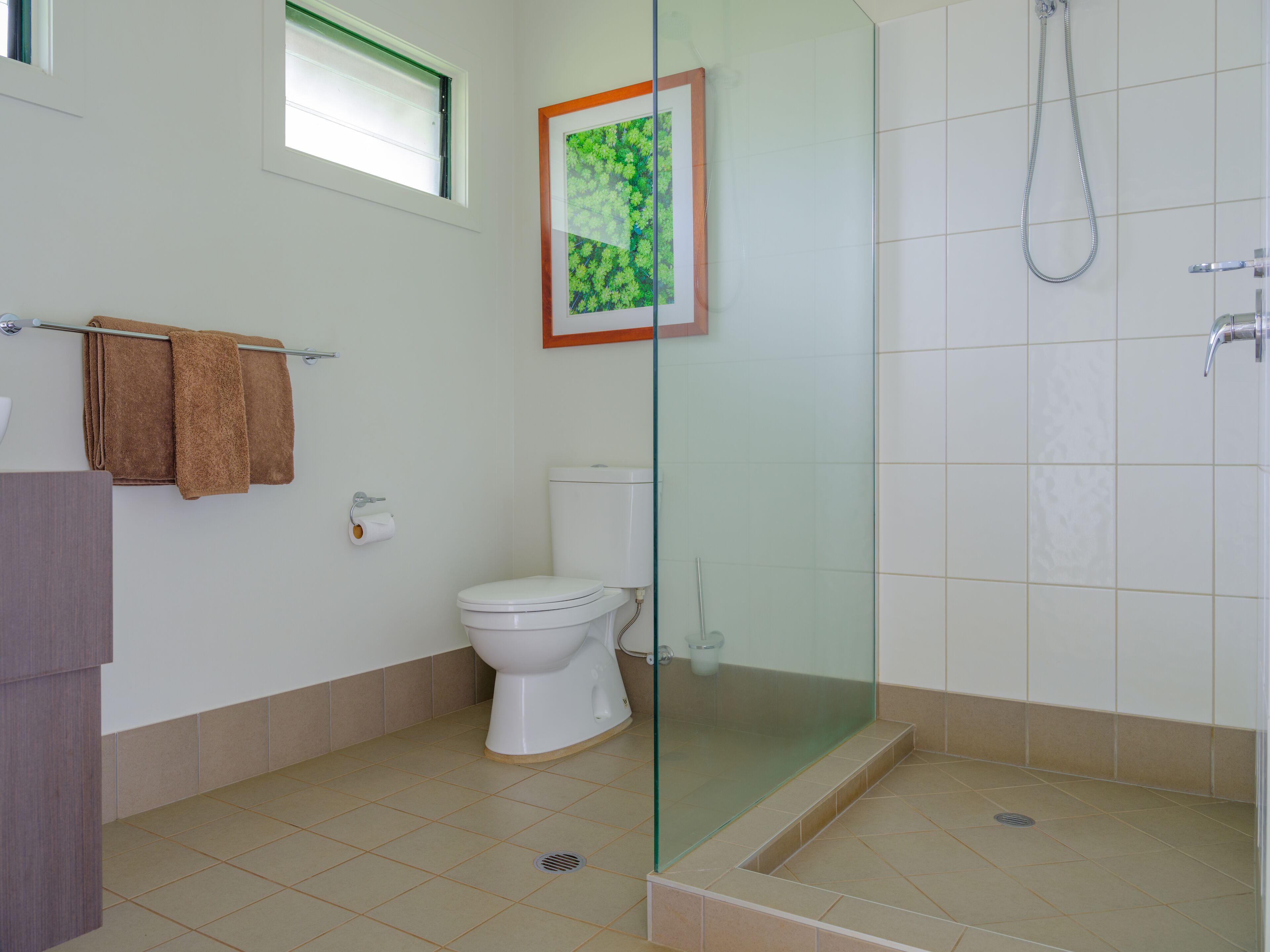 A bathroom with a toilet, a glass-enclosed shower, and a framed picture on the wall.