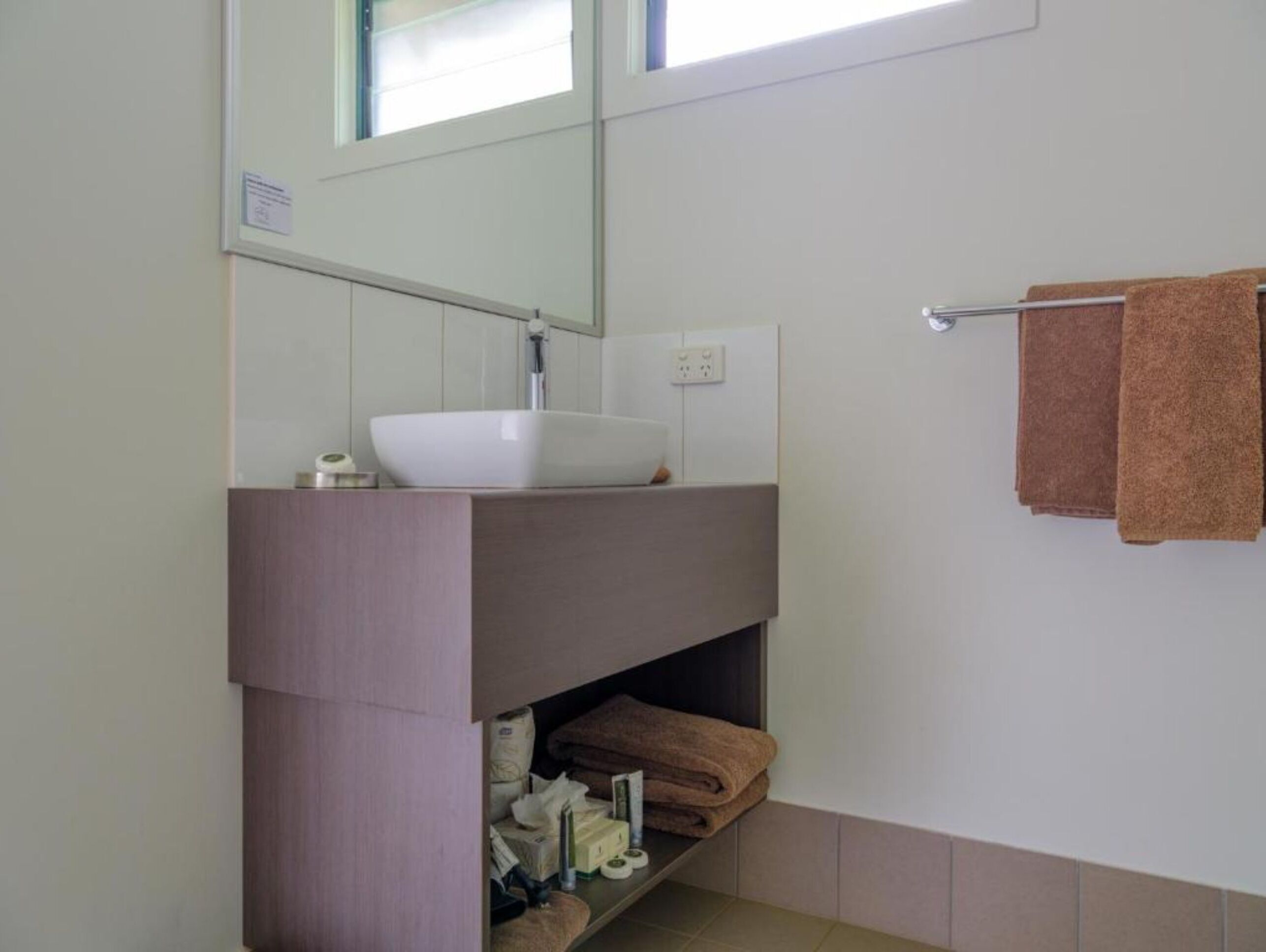 Un baño con un lavamanos blanco, un espejo y un toallero con dos toallas.